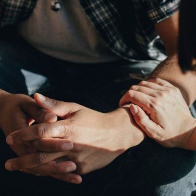 Close up of man's clenched hands with a woman's hand resting on his arm. Adobe